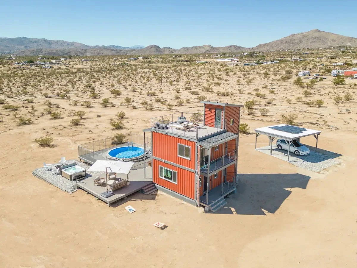 A white shipping container home in a desert landscape under a clear blue sky.