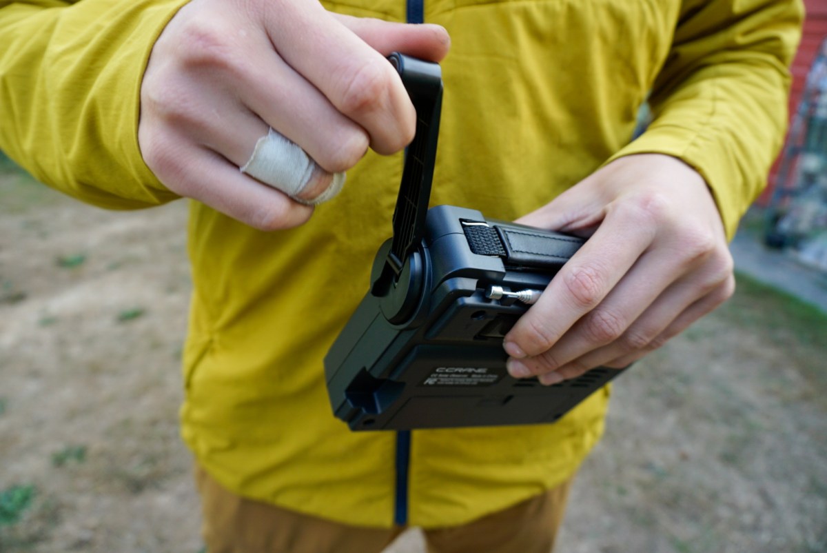 A close-up of a hand turning the integrated power crank on the side of an emergency weather radio.
