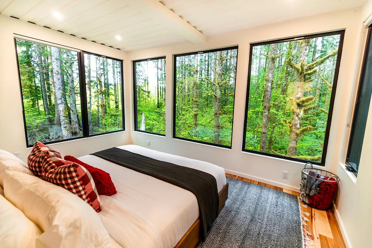 Interior view of a container home bedroom featuring a large window looking out into a forest.