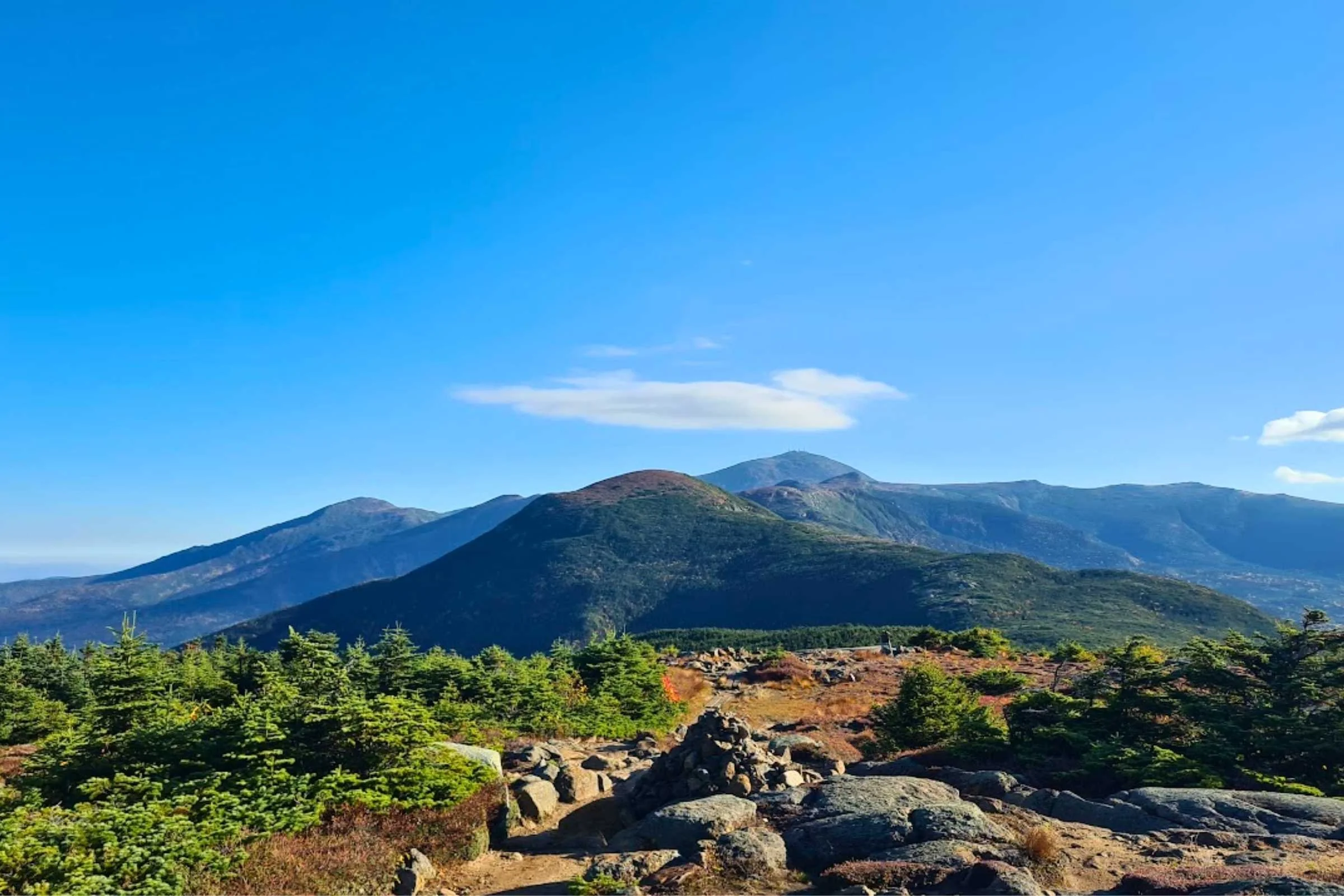 A view looking back toward the distant, cloud-capped summit of Mount Washington from Mount Pierce.