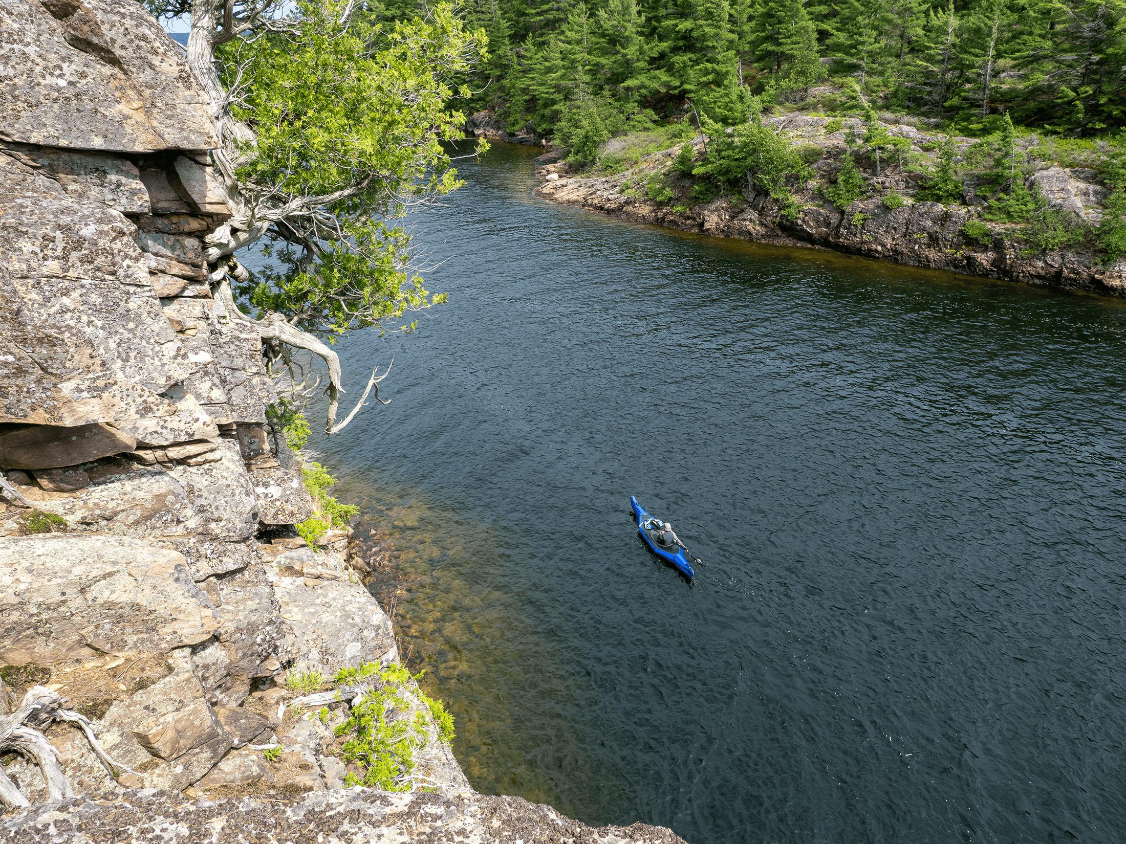 A paddler navigating the Alpacka Aleutian through a coastal channel with light chop.