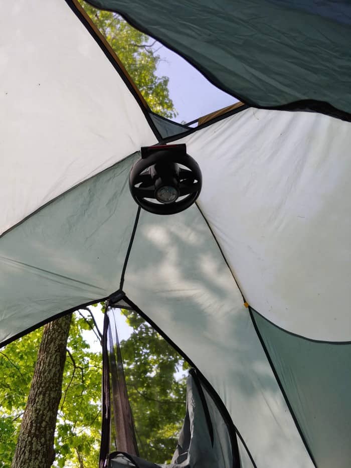 A Coleman camping fan hanging from the ceiling of a tent in the field.