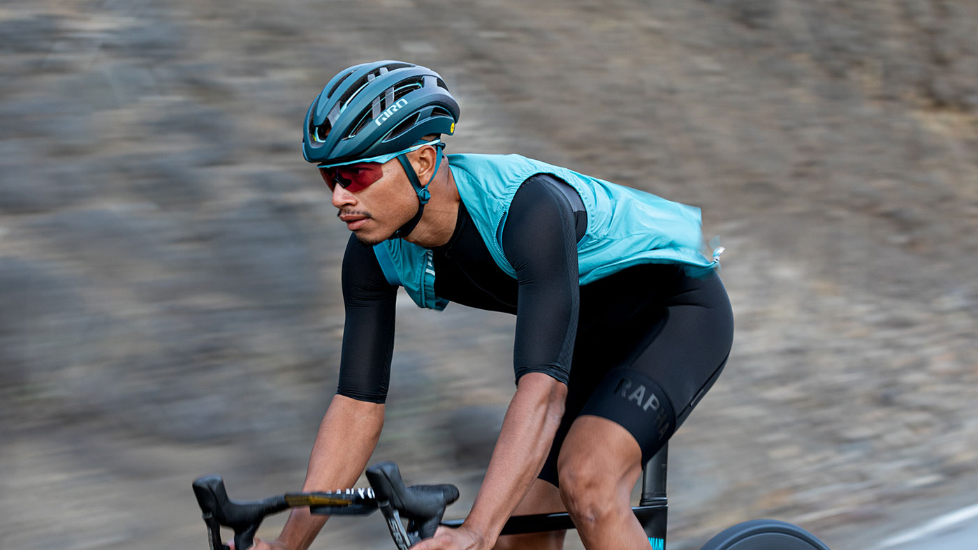 A cyclist in professional gear riding on a paved road wearing the black Giro Aries helmet.
