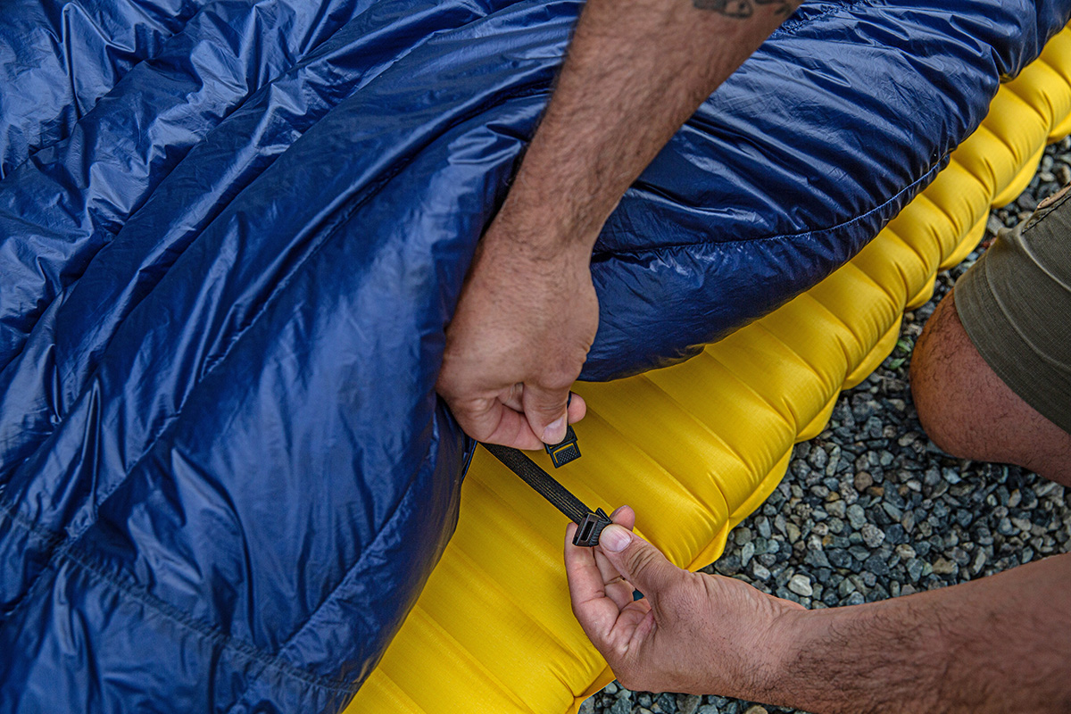 Detail of straps connecting a backpacking quilt to an inflatable sleeping pad for draft protection.