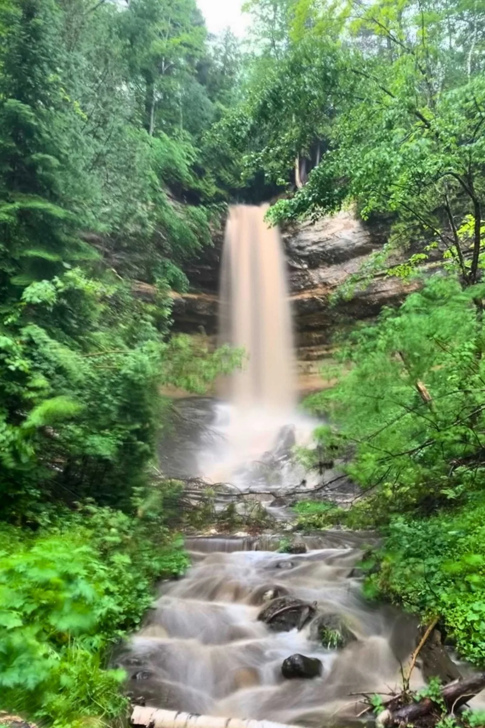 Munising Falls cascading over a sandstone cliff into a green basin.