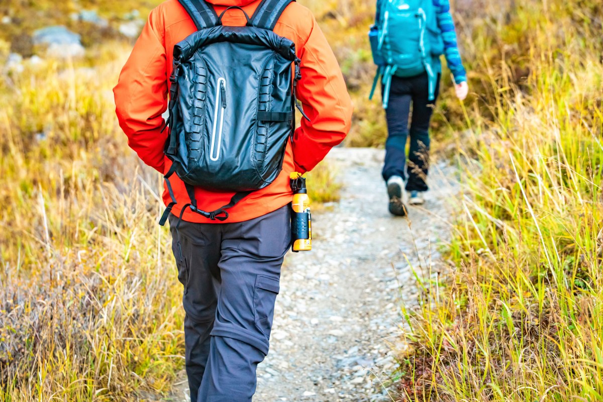A close-up of a hiker reaching for bear spray stored in an easy-access hip holster.