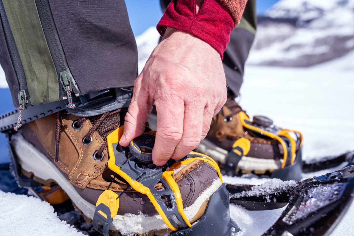 A person adjusting snowshoe bindings in winter conditions with gloves on.