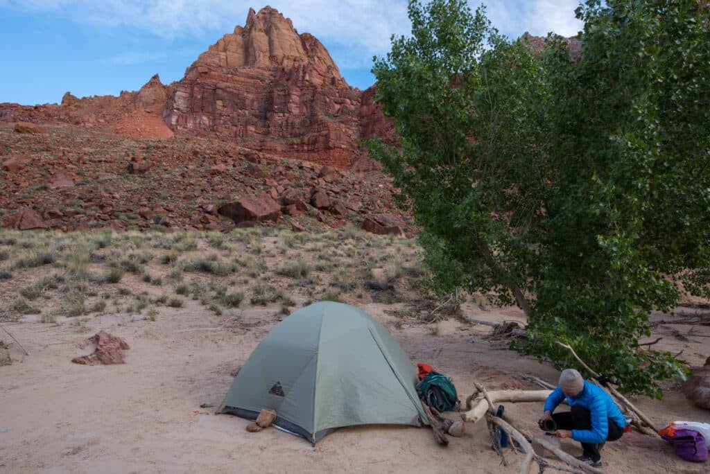 A lone tent pitched in a desert canyon, utilizing high walls for early morning shade.