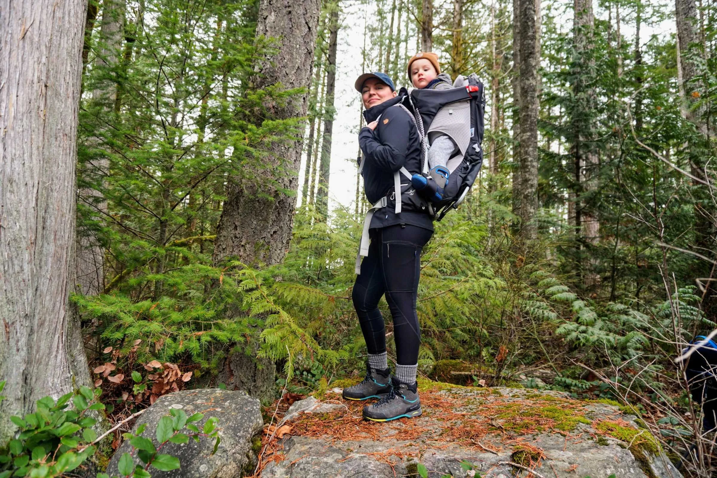A woman hiking with a toddler in a framed baby carrier through the forest in Squamish, B.C.