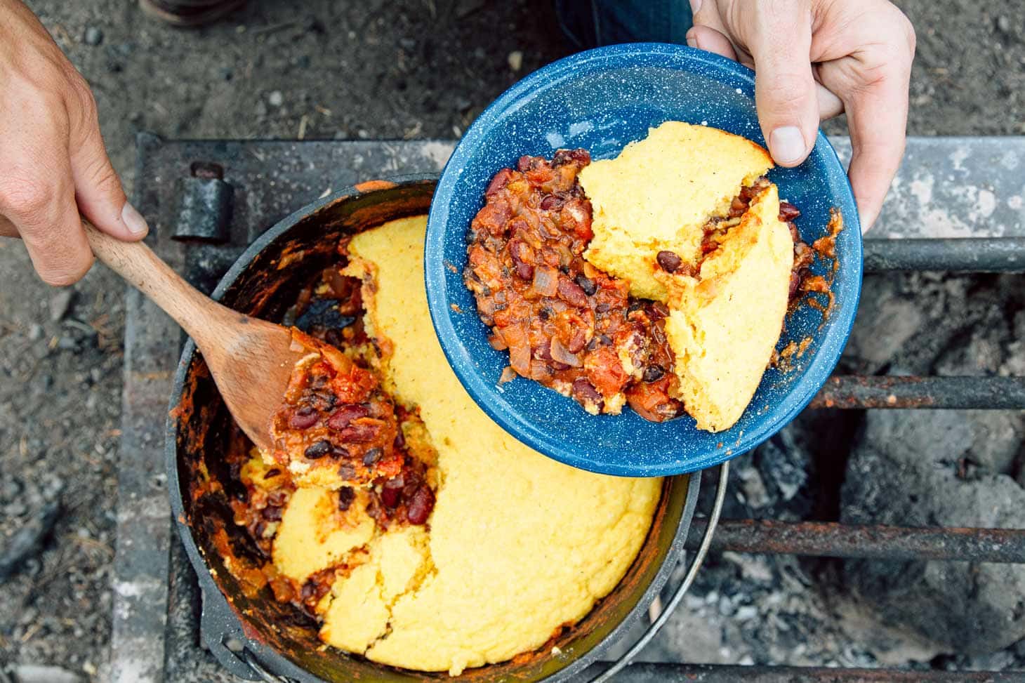 Dutch oven chili topped with a layer of golden cornbread by a campfire