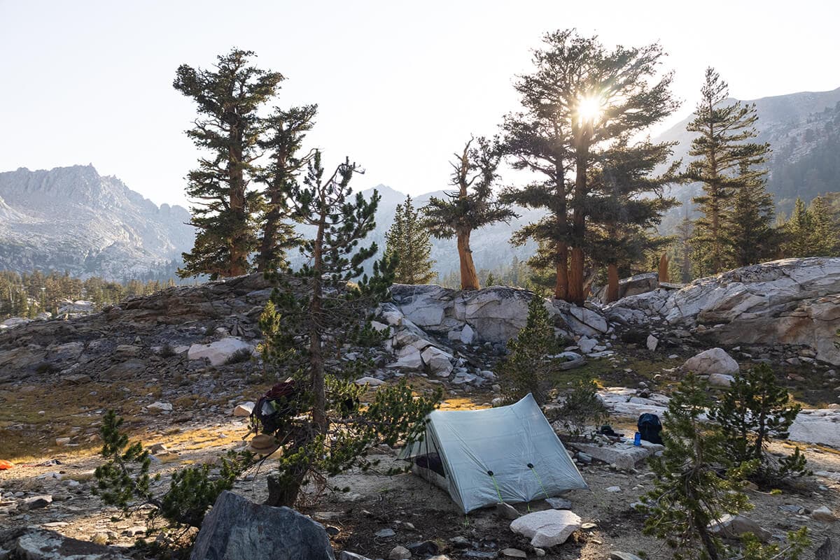A tent silhouetted against a mountain sunset, showing the completion of a camp setup.