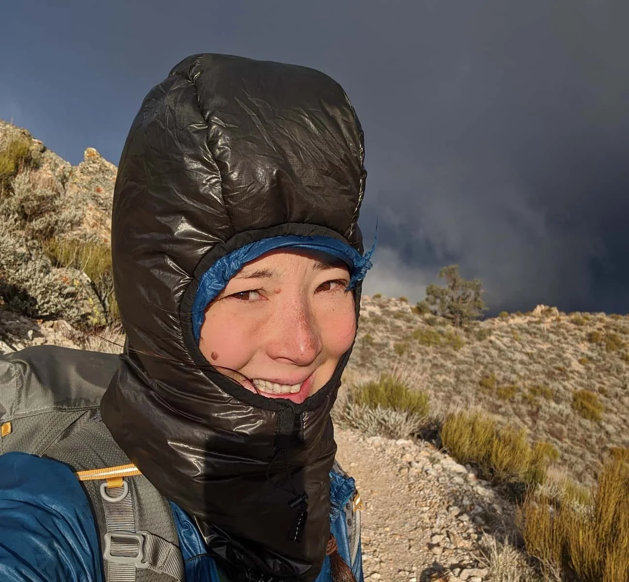 A hiker wearing a technical synthetic insulated hood in snowy or foul weather.