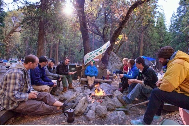 A group of campers gathering around a glowing campfire at night