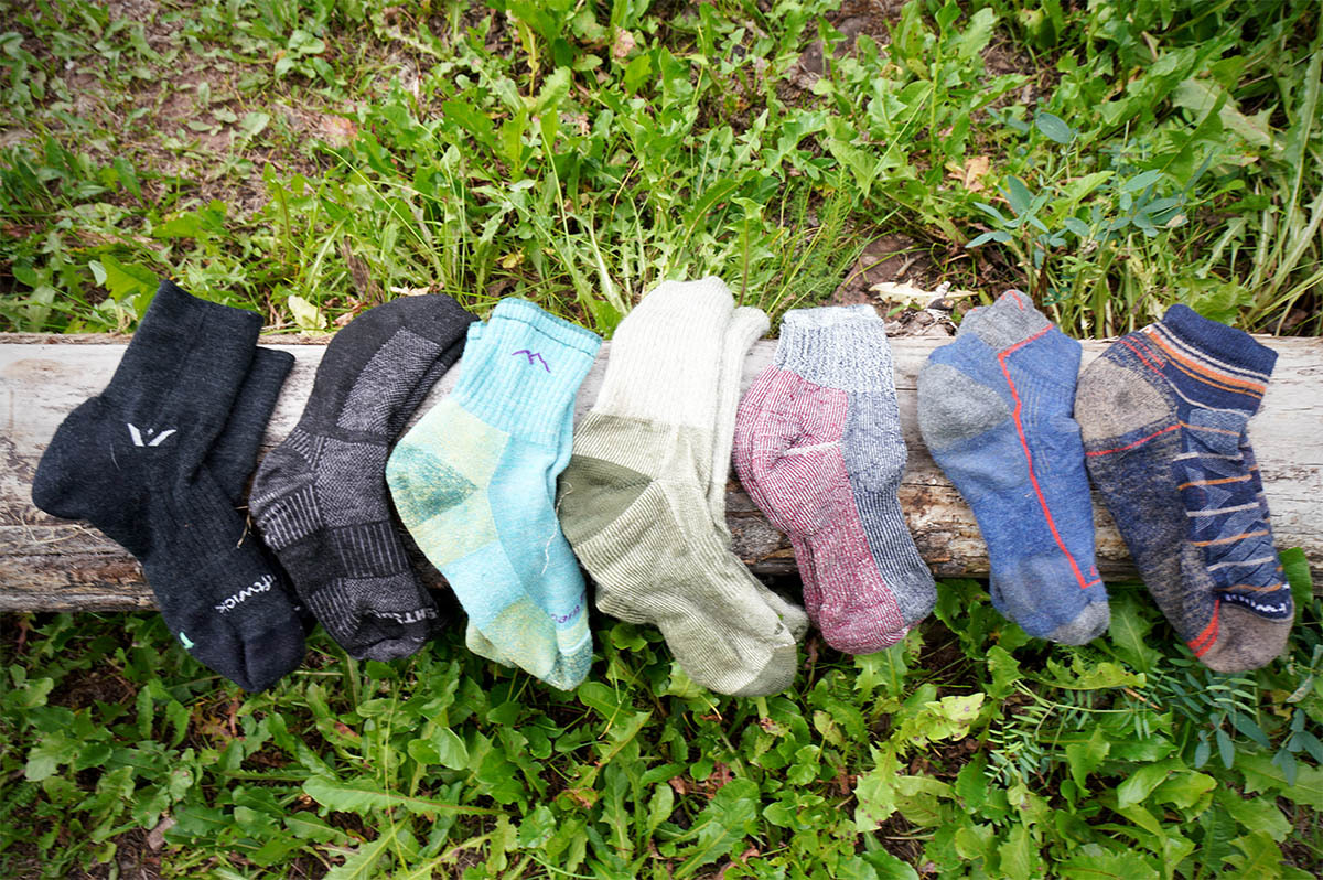 A row of various merino wool hiking socks laid out on a wooden log in the forest.