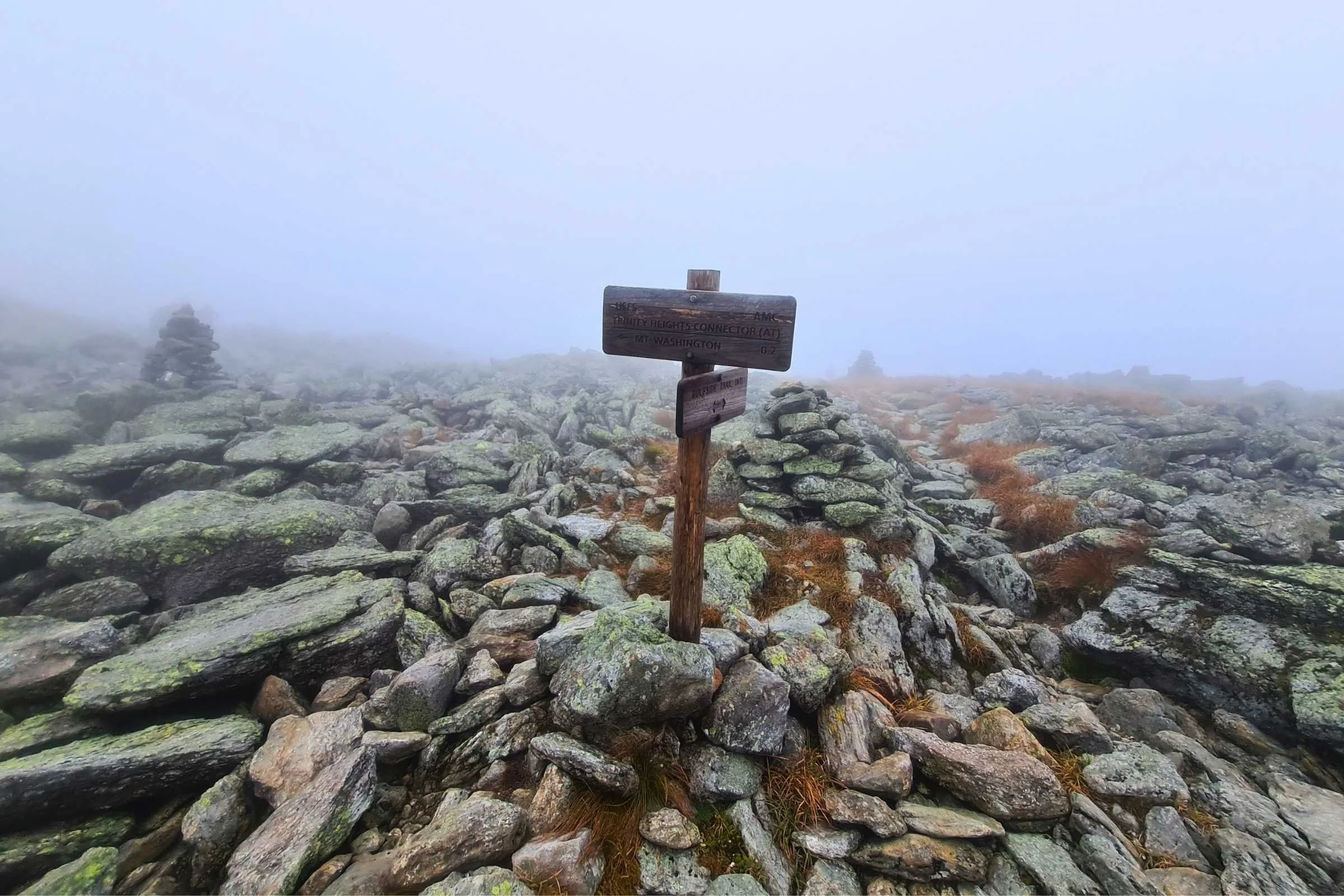 Hikers walking through dense fog and low clouds on a rocky mountain ridge.