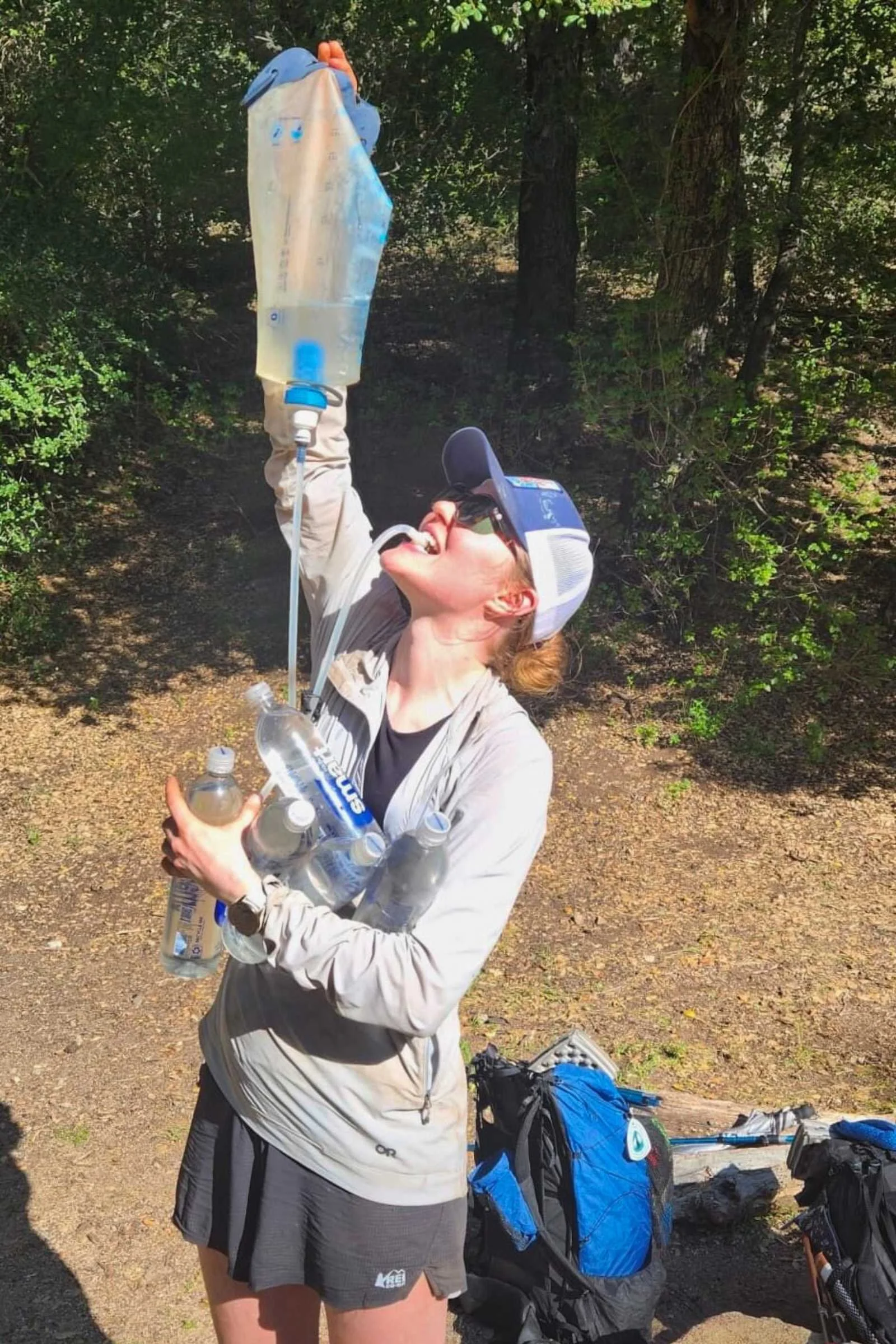 A hiker drinking water from a bottle while overlooking a mountain range.