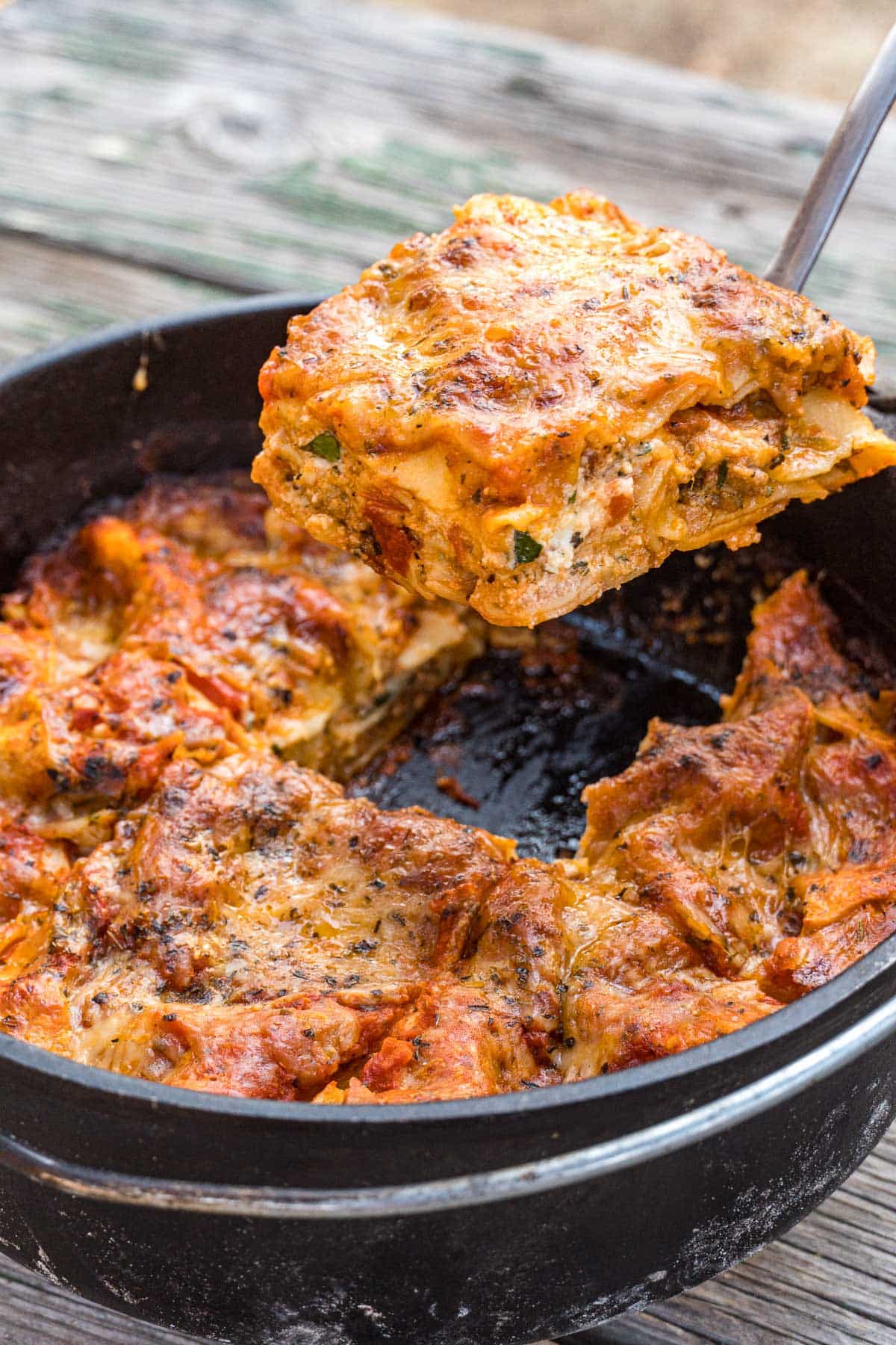 A slice of cheesy lasagna being lifted out of a cast iron Dutch oven
