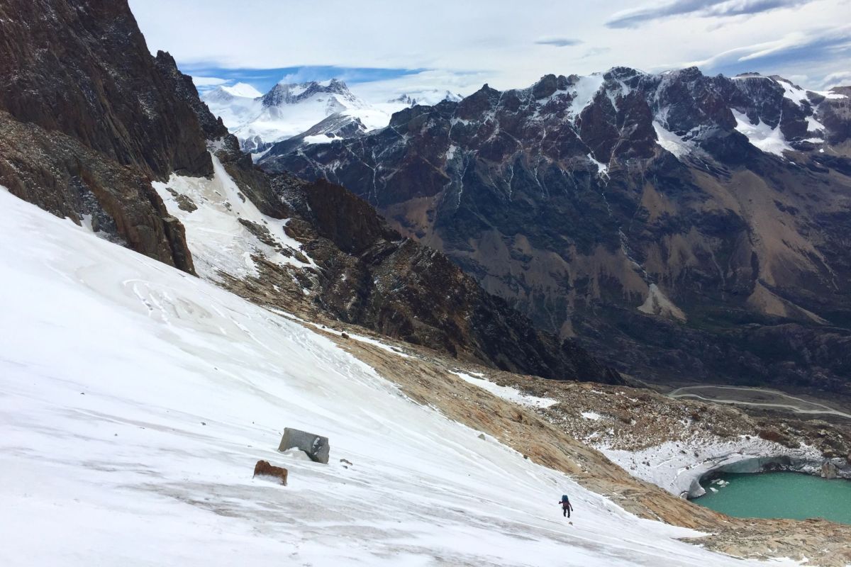 A person wearing a backpack traverses a wide mountain glacier alone.