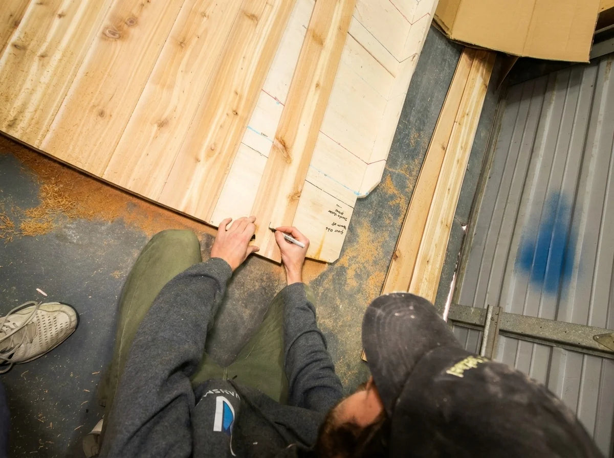 A person working on wooden storage cabinets inside a campervan shell.
