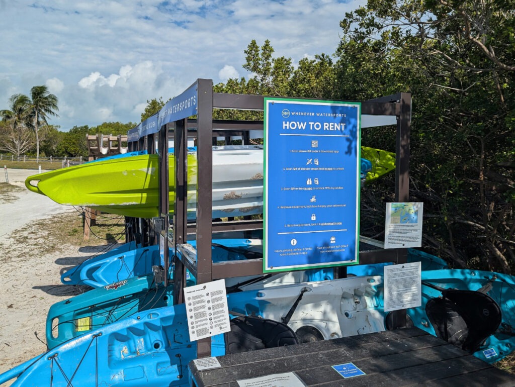 A self-serve kayak rental station with rows of kayaks and paddleboards ready for automated checkout.